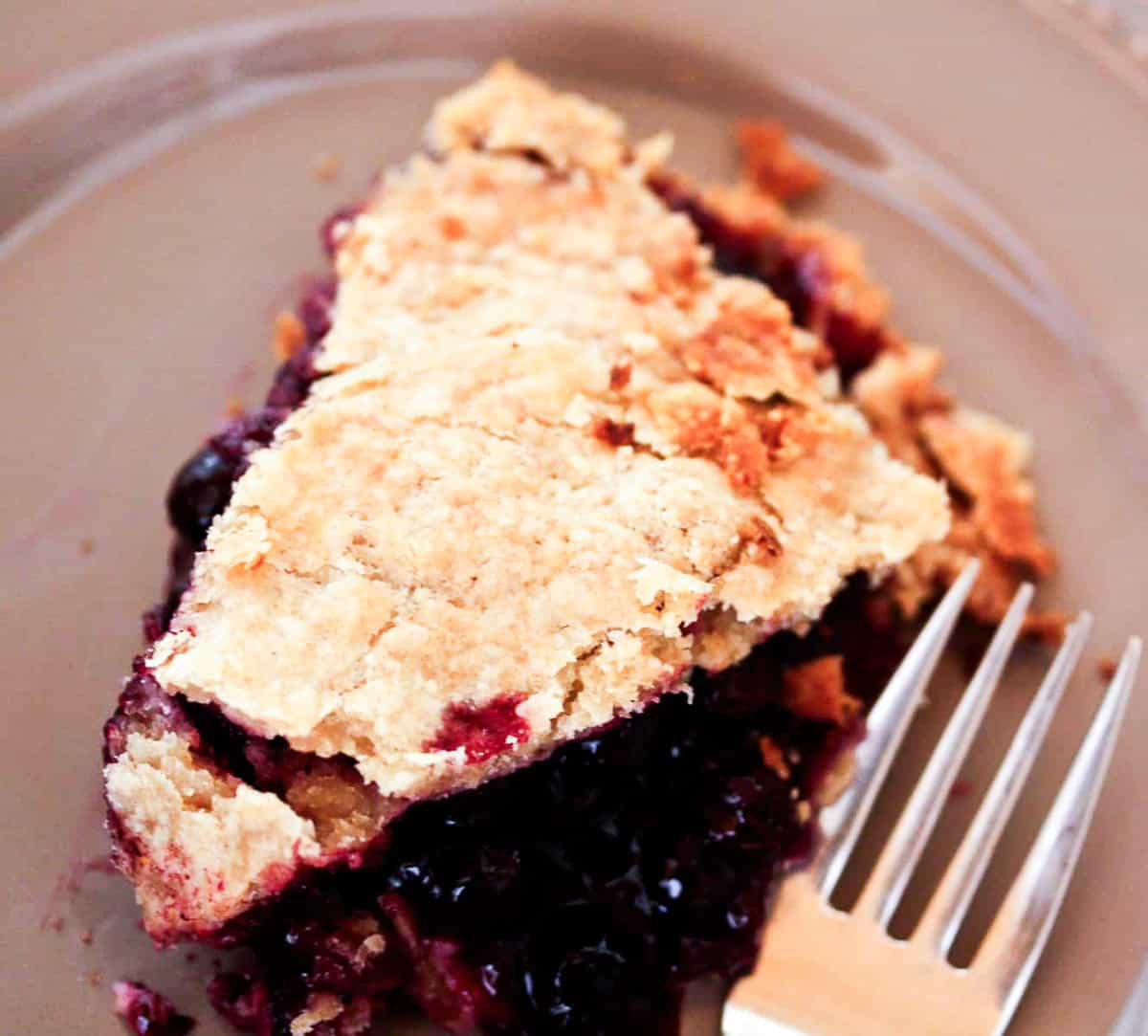 A fork rests on a plate next to a piece of blueberry blackberry pie.