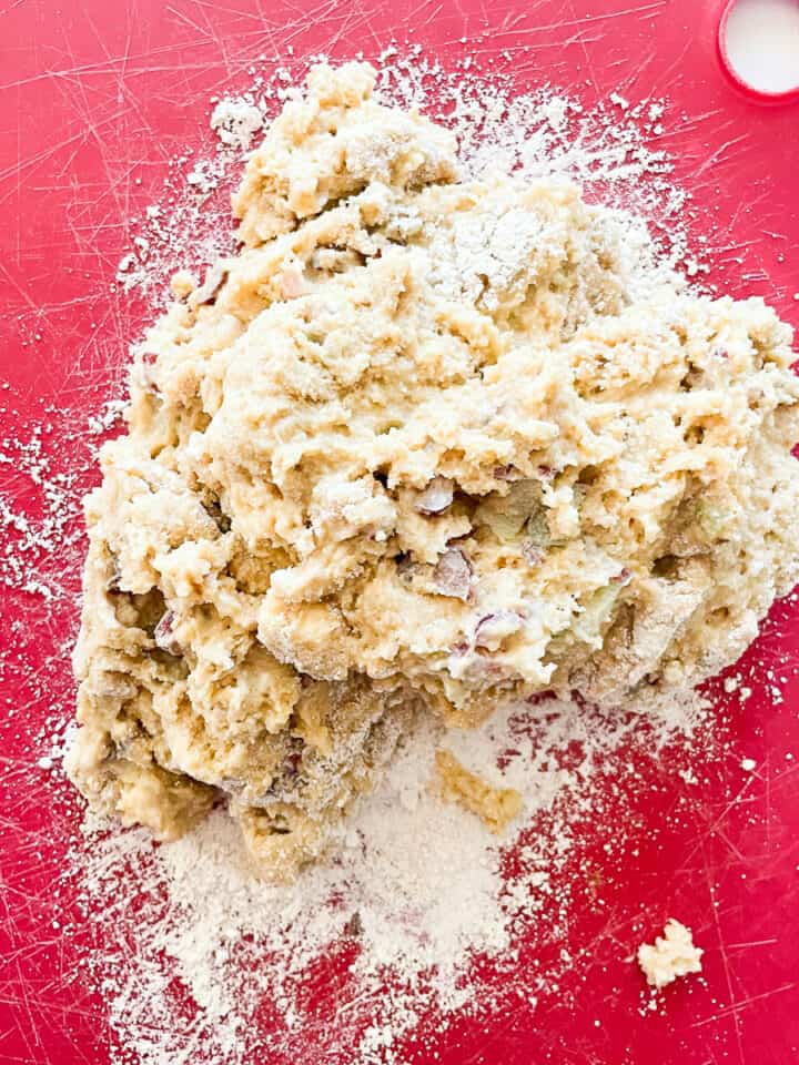 Rhubarb scone dough is turned out in a shaggy mass onto a red board.