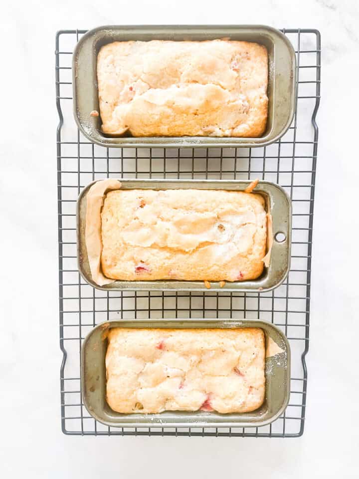 Three mini loaves of gluten free strawberry rhubarb bread cool on a wire rack.