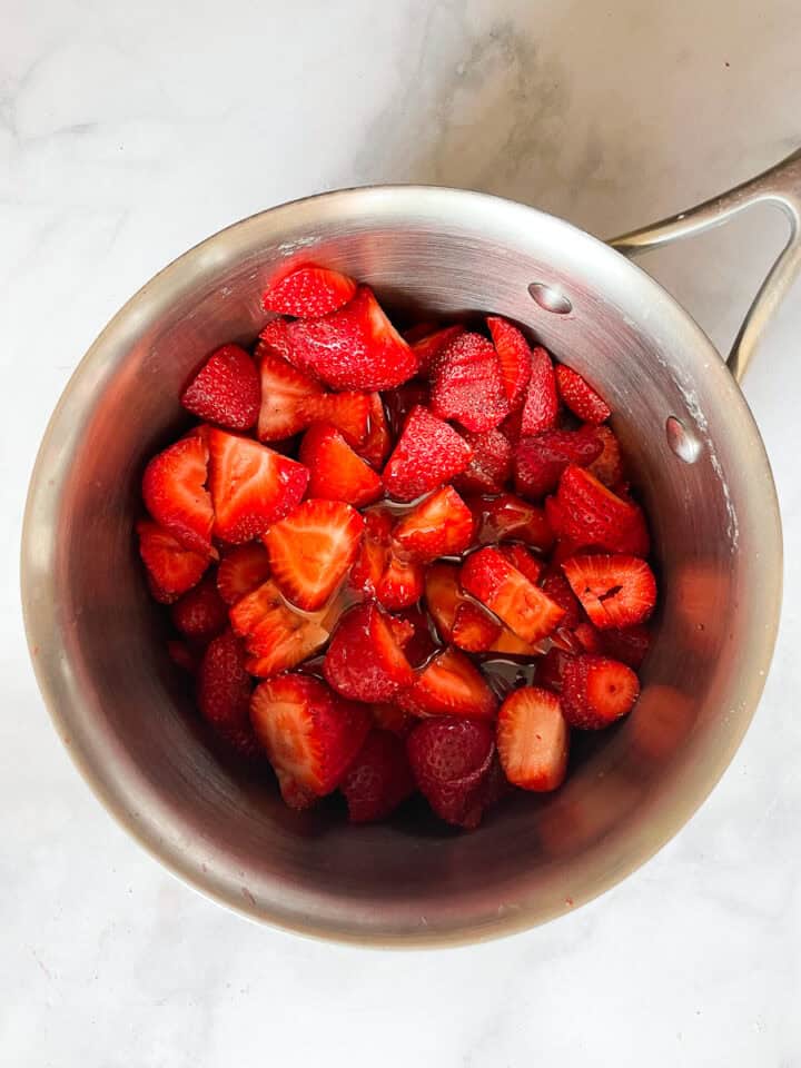 Strawberries and honey are added to a pot.