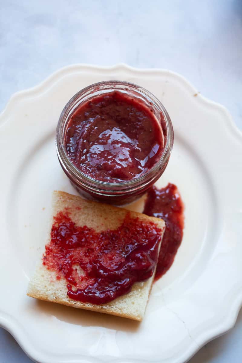 A jar of strawberry honey jam with jam on bread.