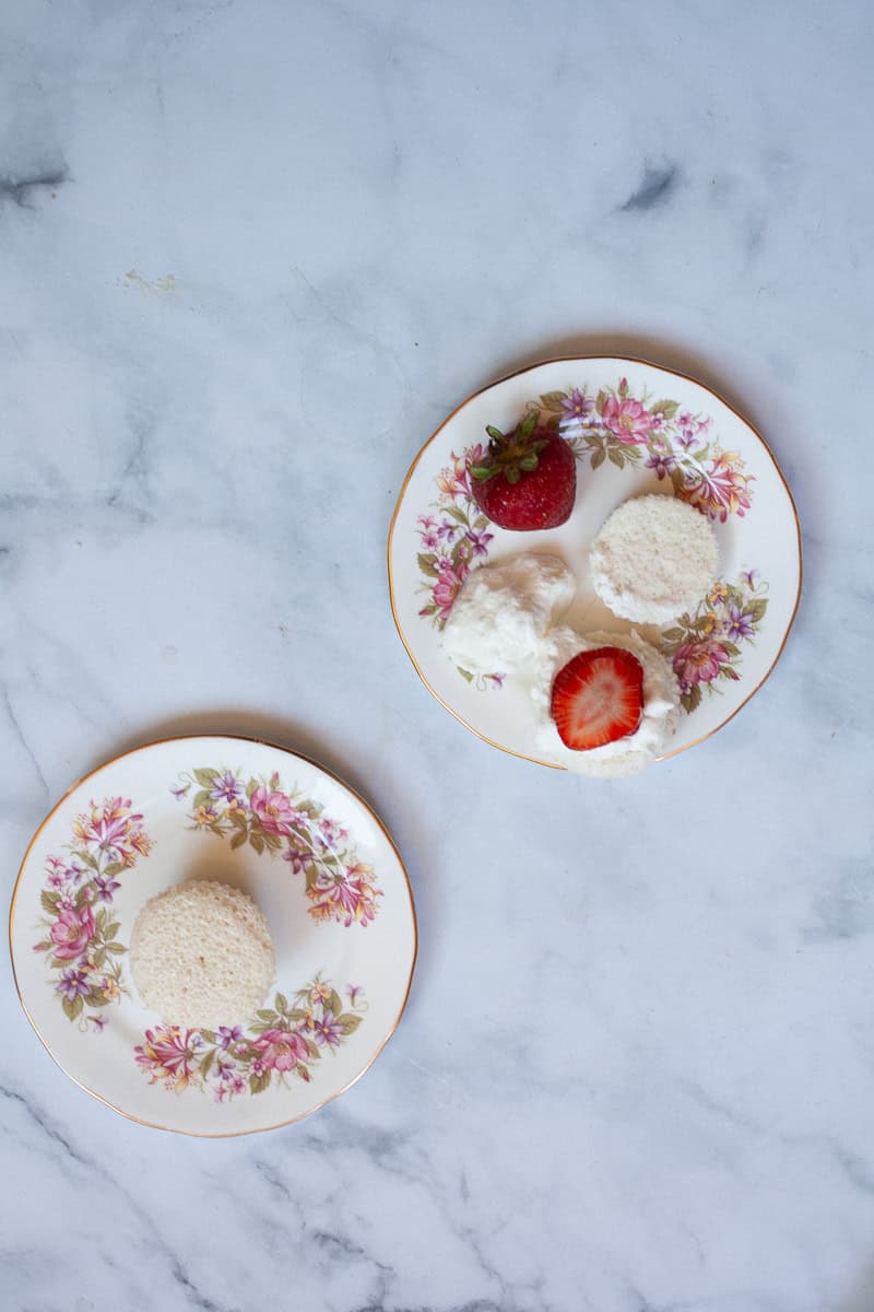 An angel food cupcake on a plate with another one on a plate with strawberry and whipped cream.