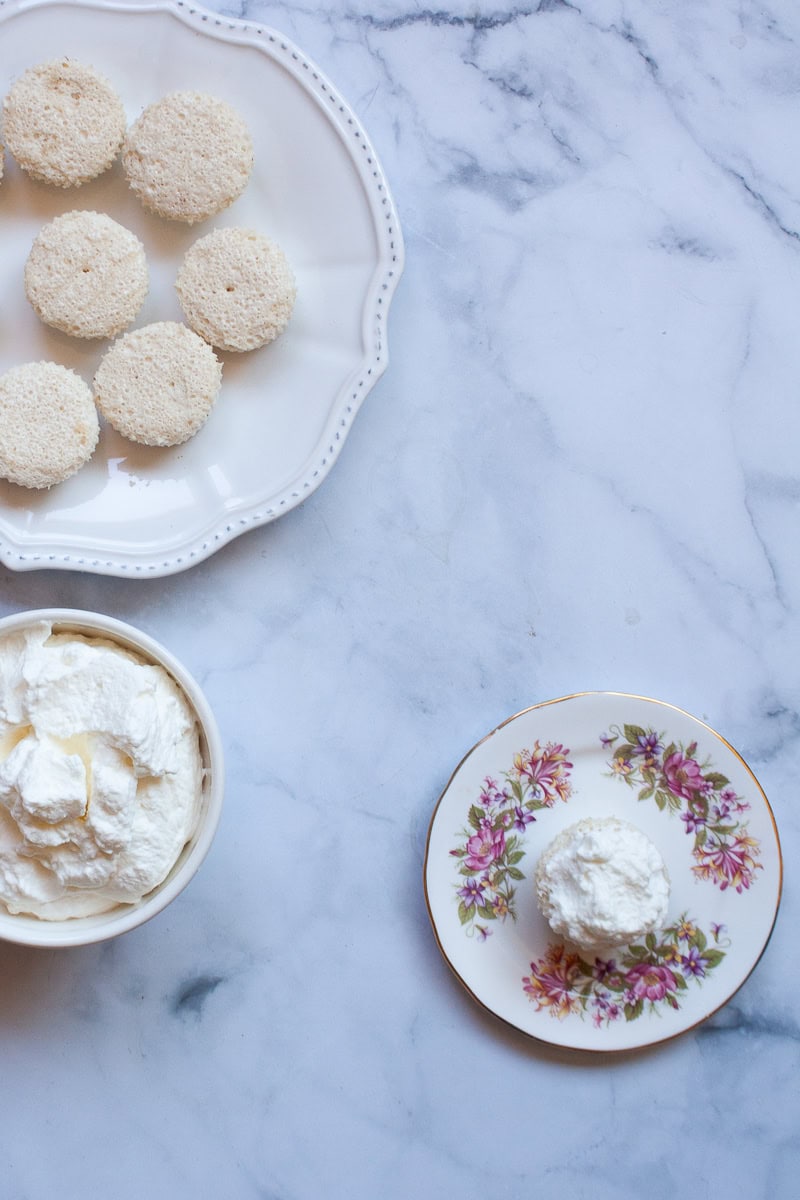 Angel food cupcakes next to a bowl of whipped cream.