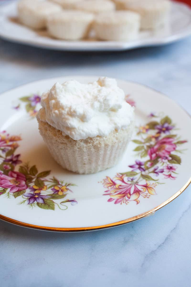 Whipped cream tops an angel food cupcake on a plate with cupcakes in the background.