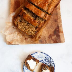 A brown loaf of oat flour banana bread cut into slices next to a slice of bread.