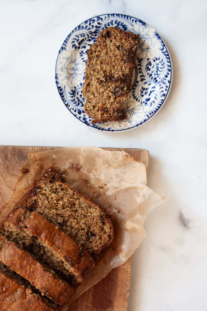 A slice of banana bread on a plate next to a loaf of bread.