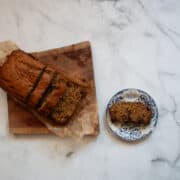 A slice of banana bread on a plate next to a loaf of bread.