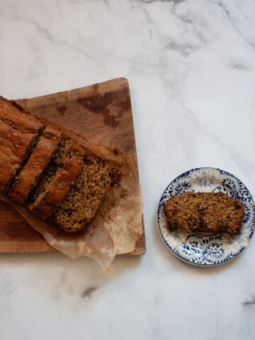 A slice of banana bread on a plate next to a loaf of bread.