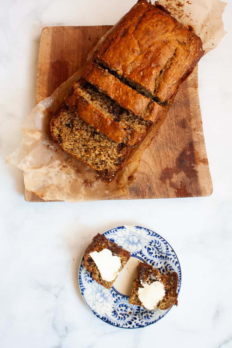 A brown loaf of oat flour banana bread cut into slices next to a slice of bread.