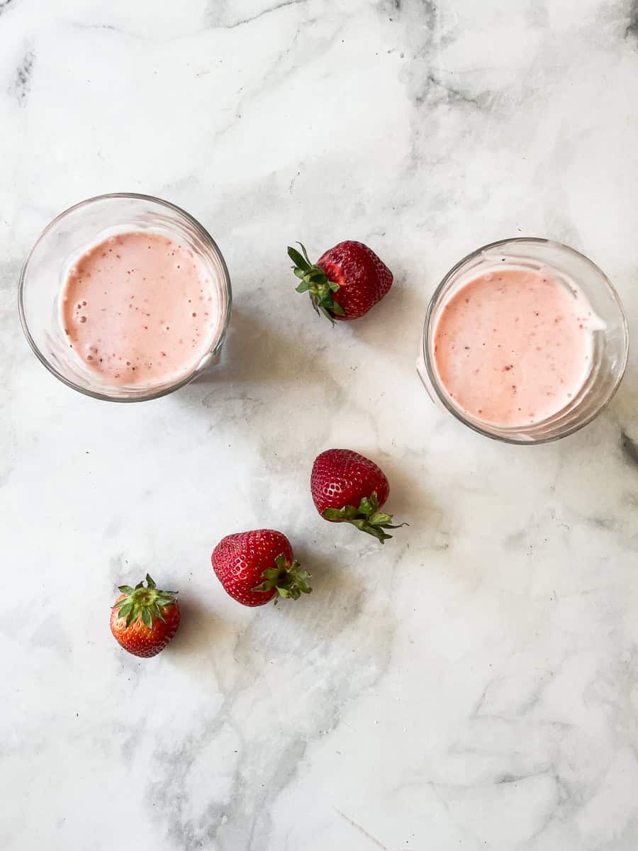 Glasses of banana strawberry smoothie with strawberries scattered around them.