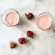 Glasses of banana strawberry smoothie with strawberries scattered around them.