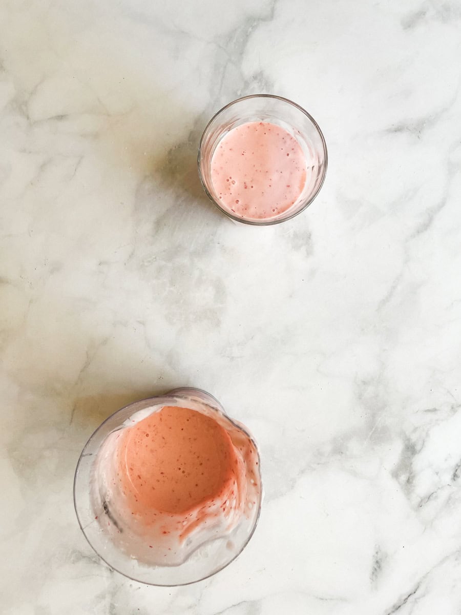 A glass of banana strawberry smoothie and the smoothie in the blender.