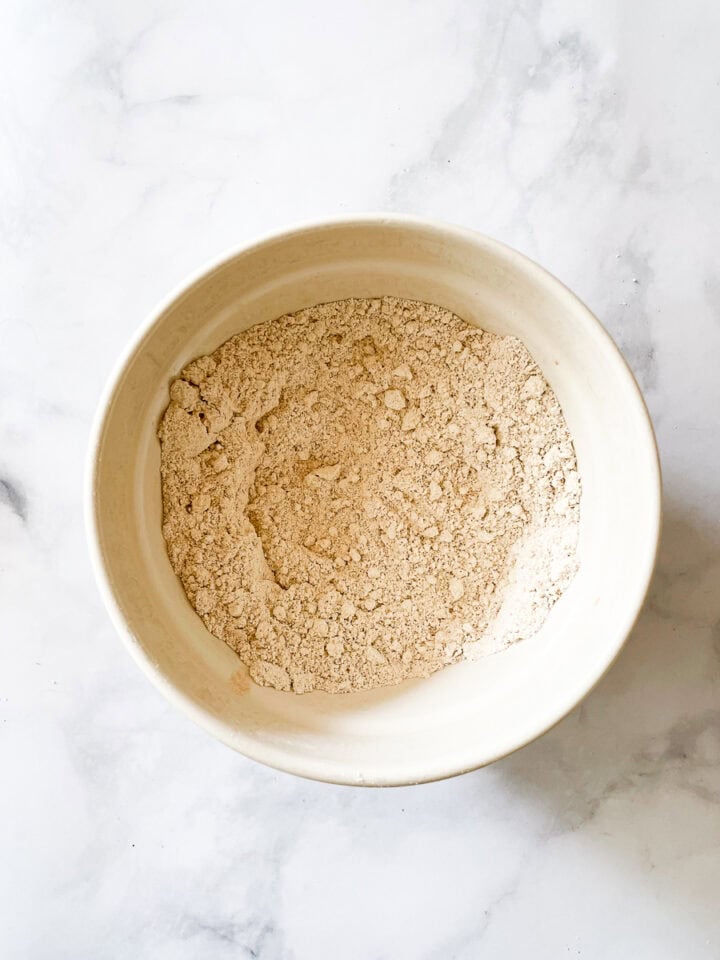 Oat flour, baking powder, spices, and salt are mixed in a large bowl.