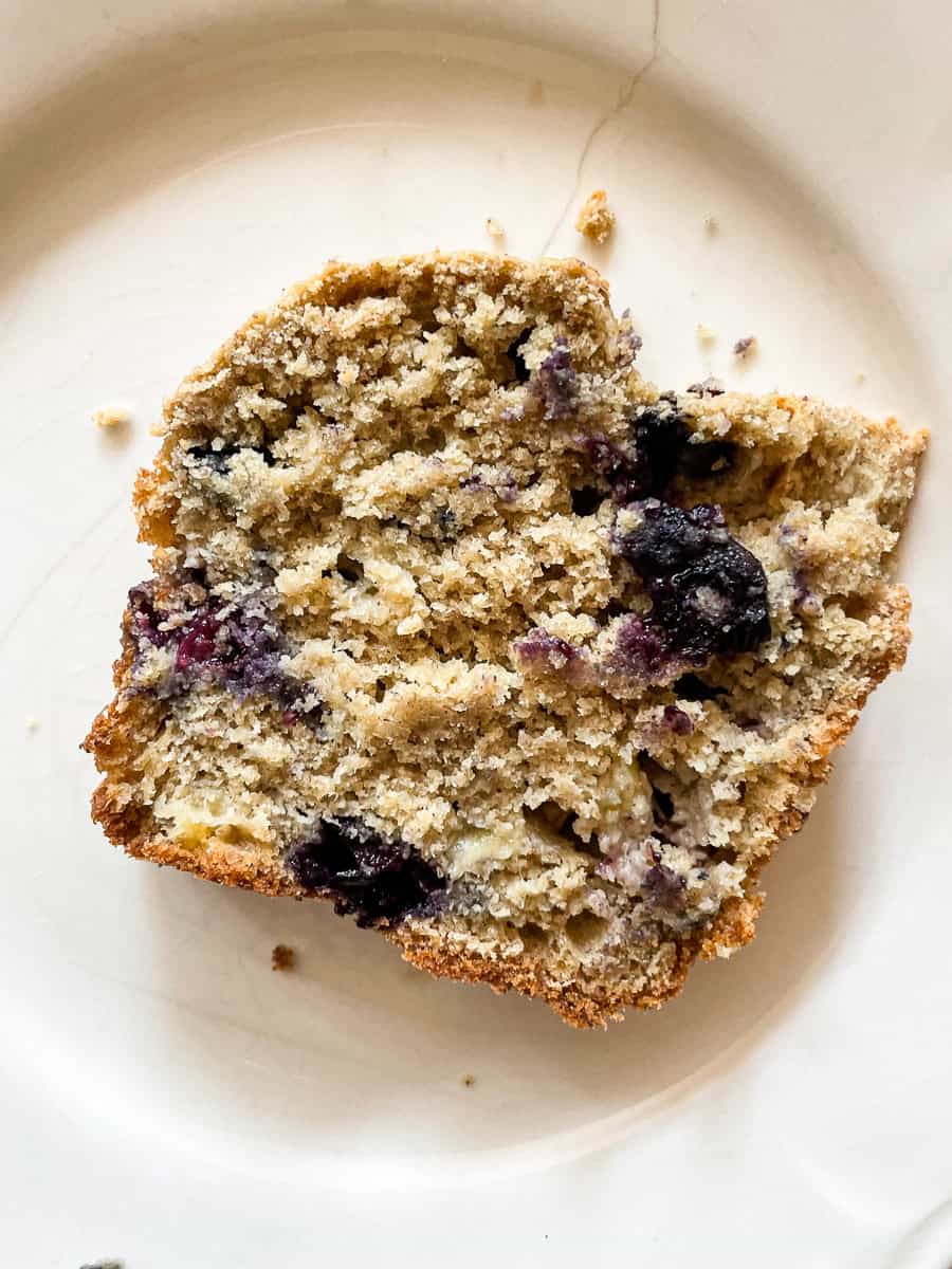 Blueberries peek out of a piece of blueberry banana bread on a plate.