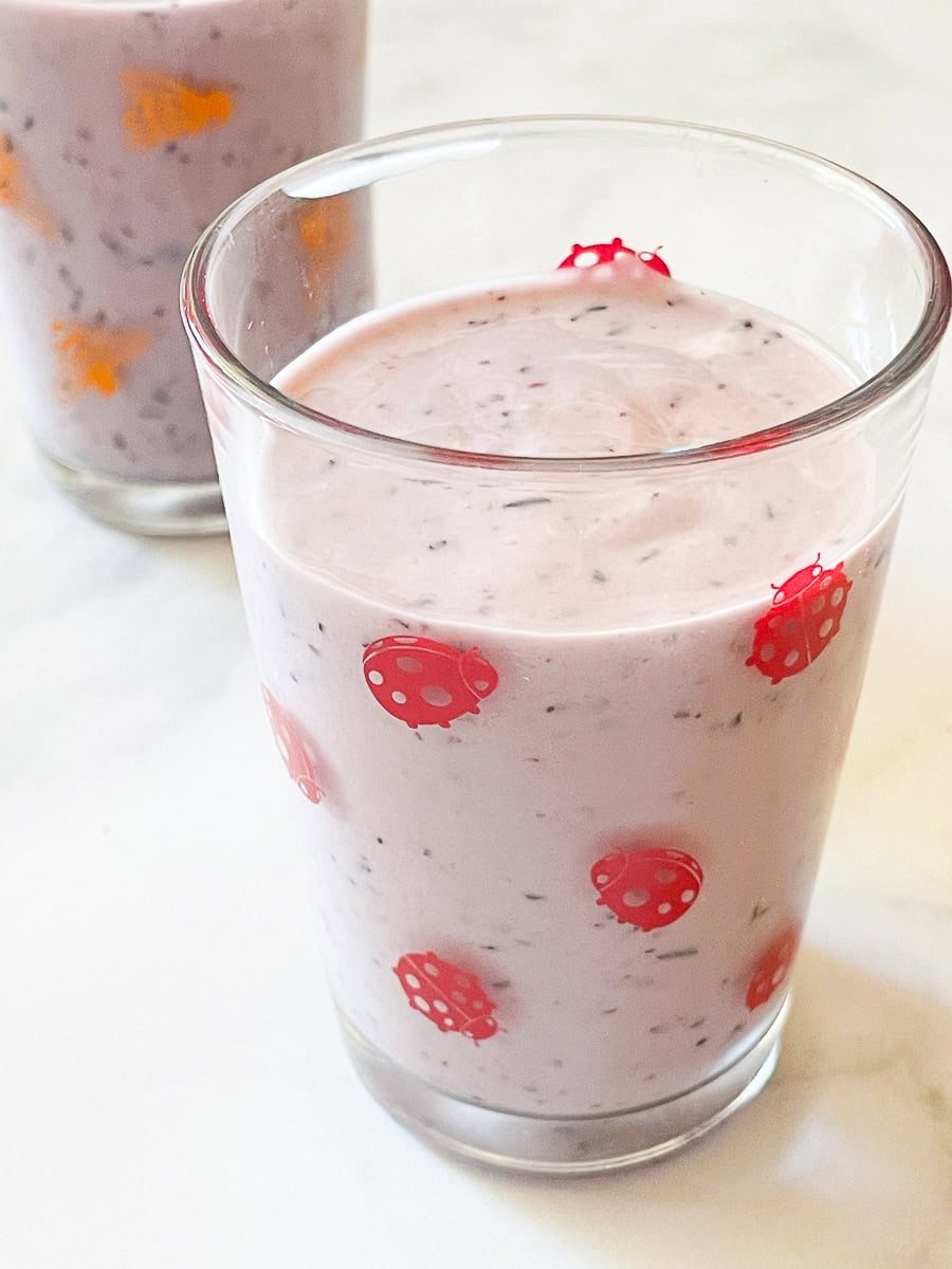 A blueberry banana smoothie in a ladybug glass.