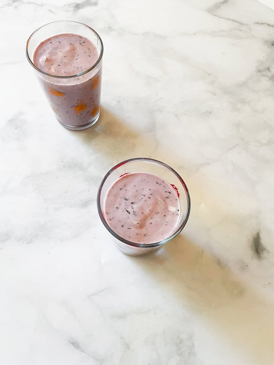 Two glasses of blueberry banana smoothie on a white counter.