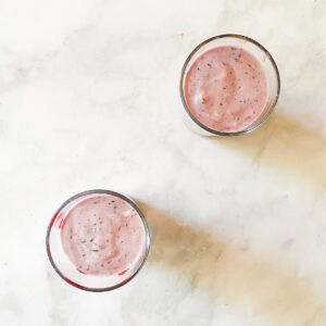 Two glasses of blueberry banana smoothie on a white counter.