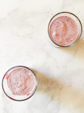Two glasses of blueberry banana smoothie on a white counter.