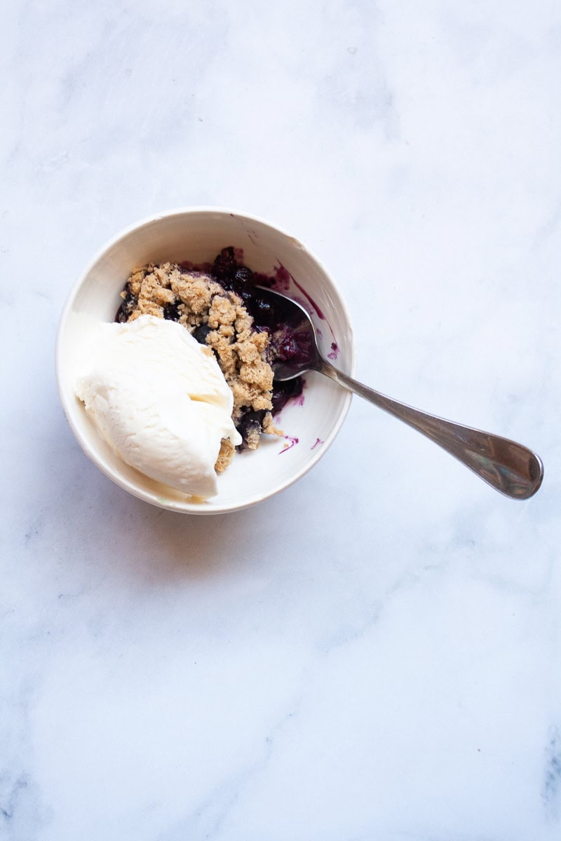 Blueberry crisp is served in a bowl with a scoop of ice cream.