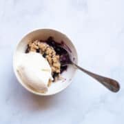 A bowl of gluten free blueberry crisp with vanilla ice cream.
