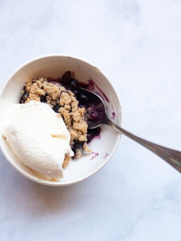 A bowl of gluten free blueberry crisp with vanilla ice cream.