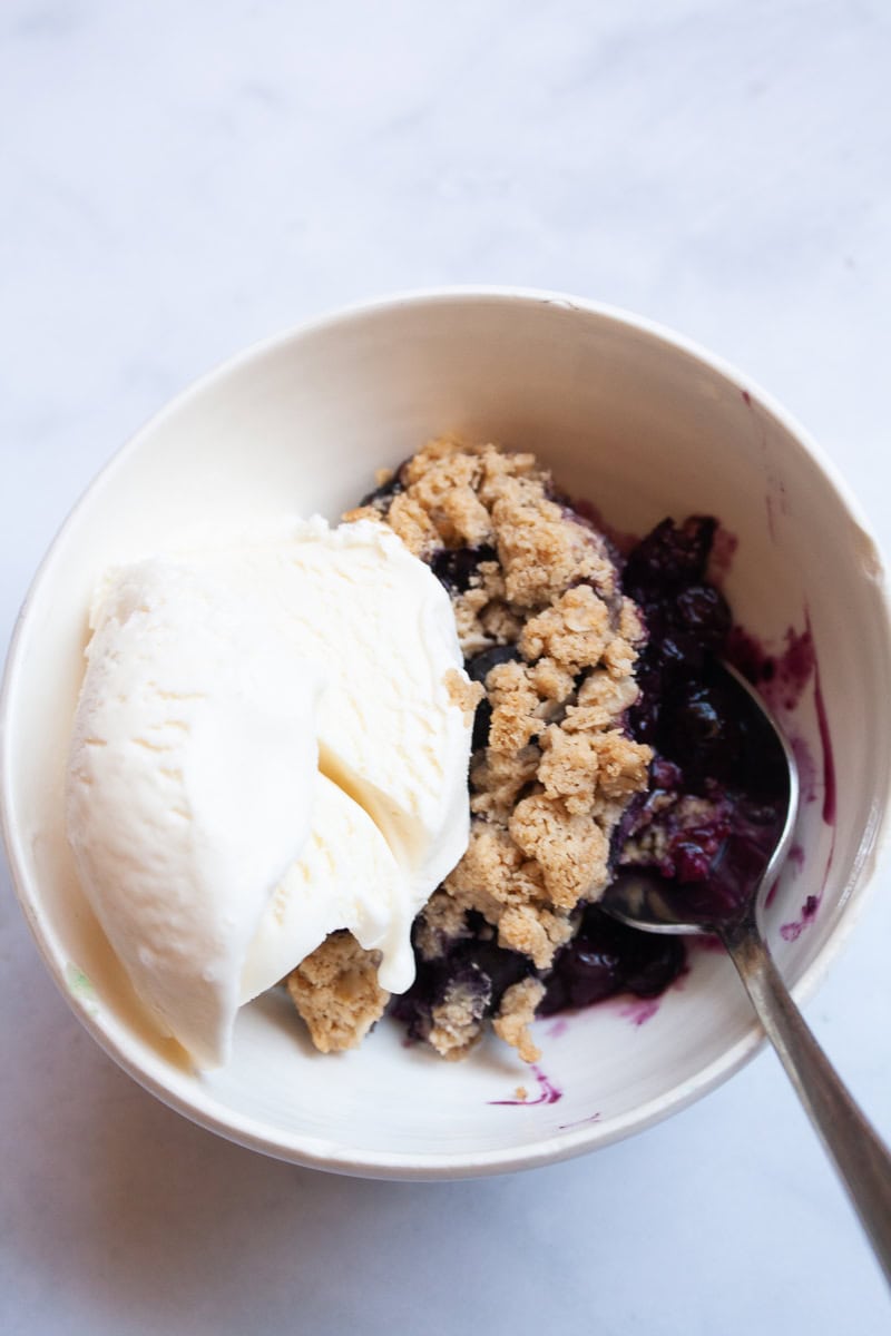 A bowl of gluten free blueberry crisp with vanilla ice cream.