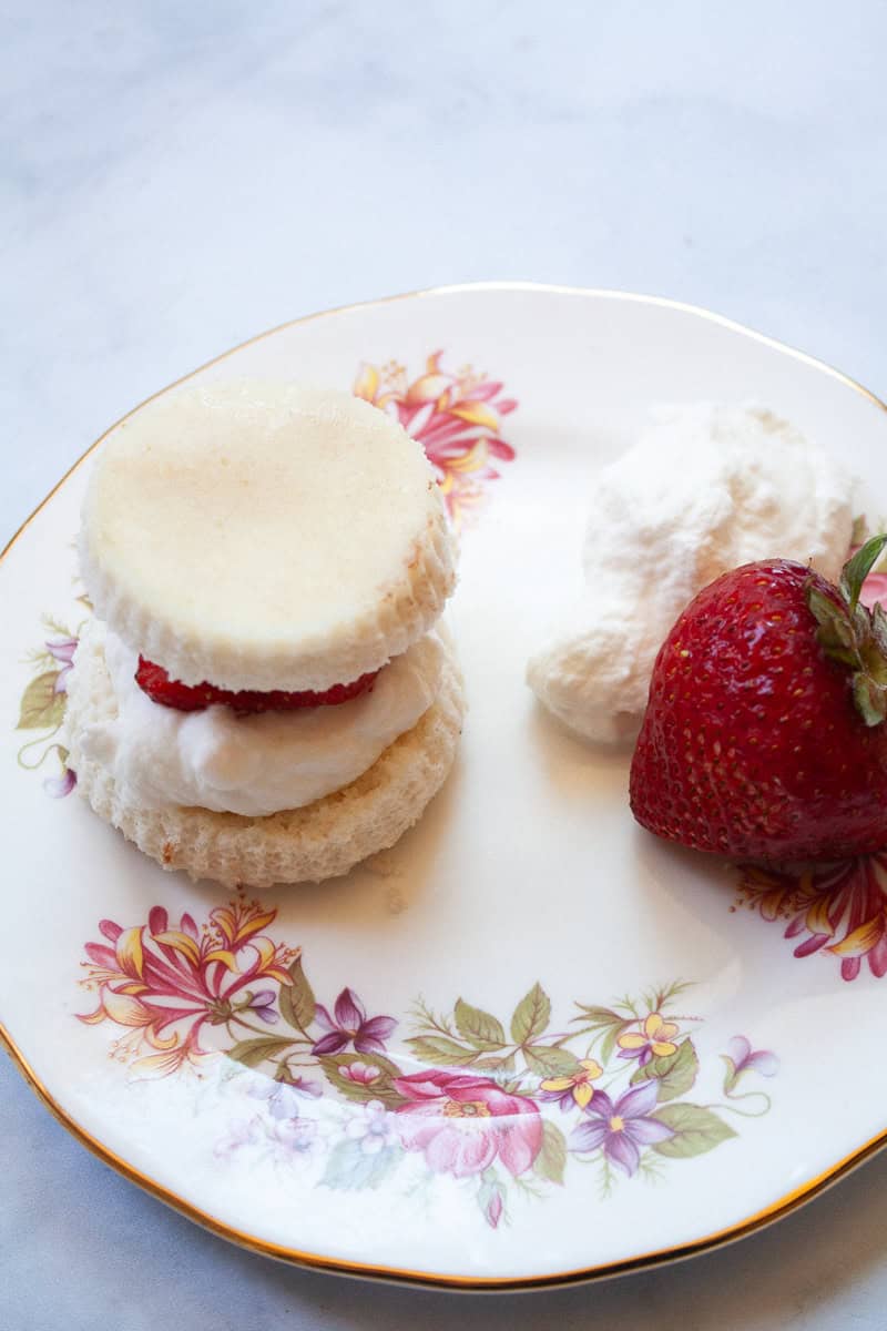 Gluten free strawberry shortcakes on a plate next to a strawberry.