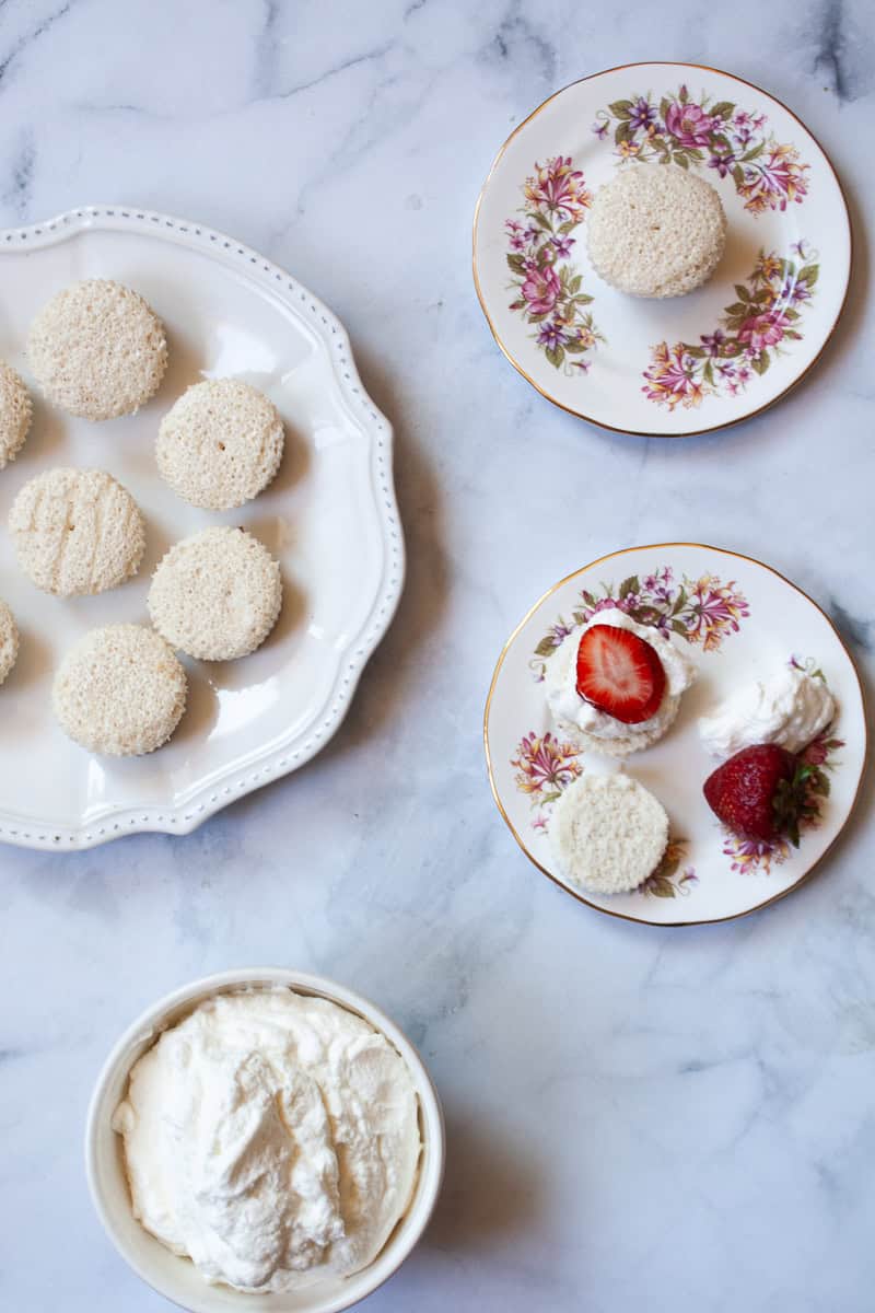 Little gluten free cakes on a plate next to plates of gluten free strawberry shortcakes.