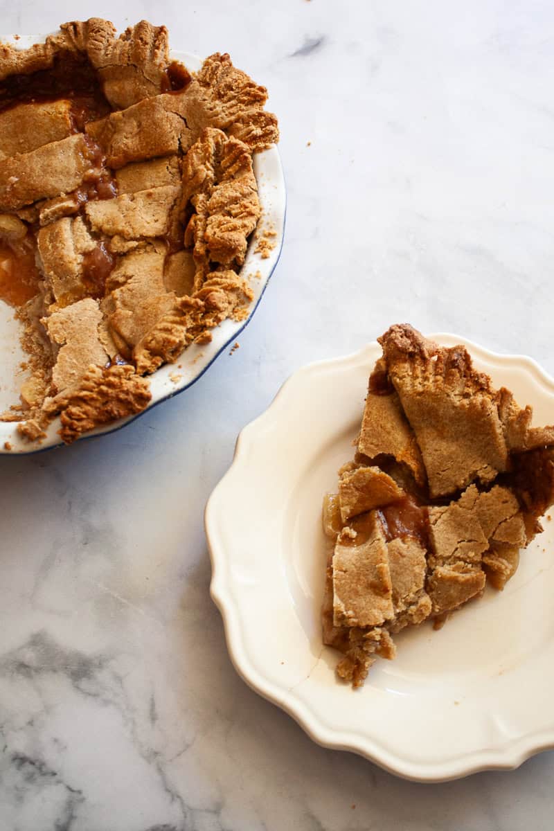 A slice of peach pie on a white plate with the pie to the left of it.