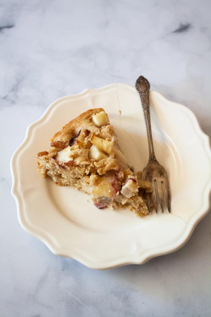 A fork rests alongside a slice of peach cake on a plate.