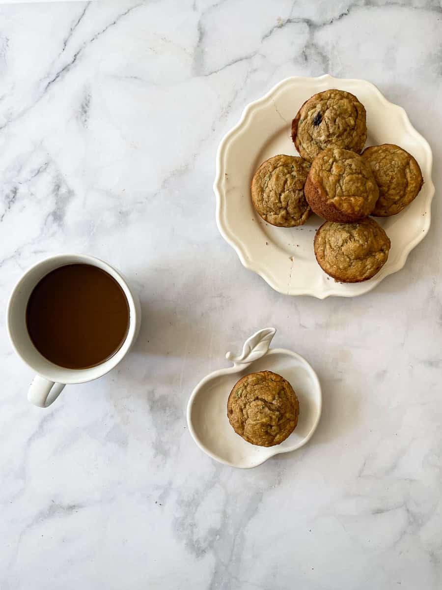 A cup of coffee, a banana zucchini muffin, and a plate of muffins.