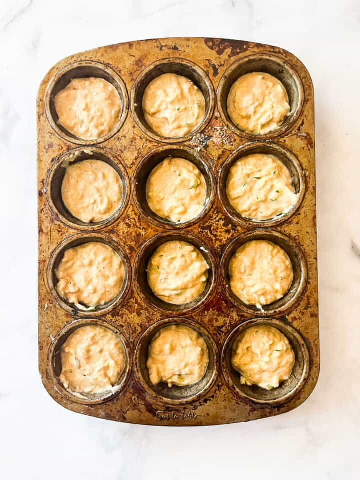 Batter for gluten free banana zucchini muffins rests in a muffin tin.