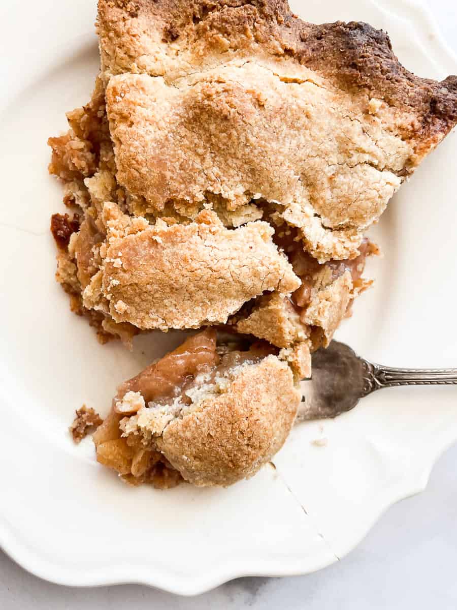 A fork cuts into a piece of gluten free Gravenstein apple pie on a plate.