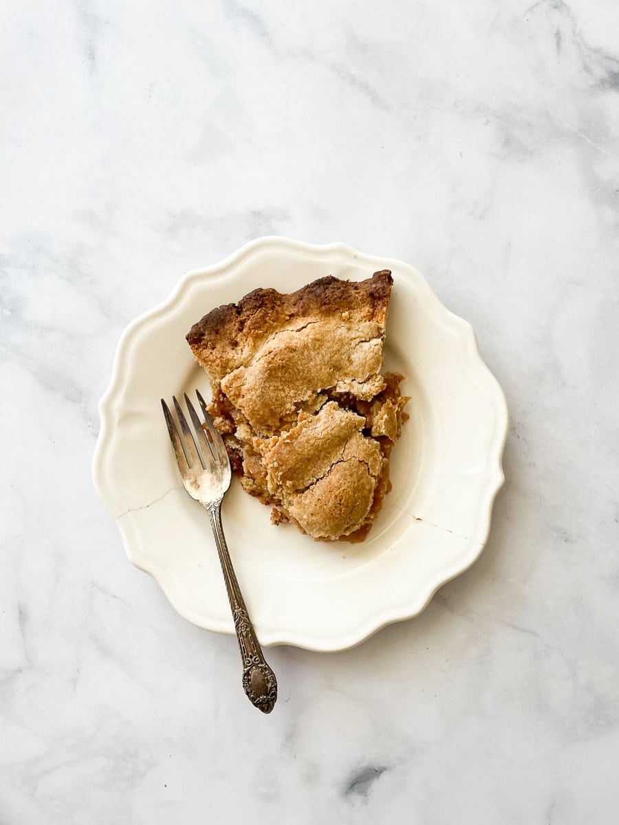 A slice of gluten free Gravenstein apple pie on a white plate with a fork.