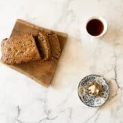 A loaf of gluten-free zucchini bread on a board with a plate and a slice and a cup of tea.