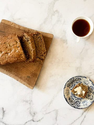 A loaf of gluten-free zucchini bread on a board with a plate and a slice and a cup of tea.