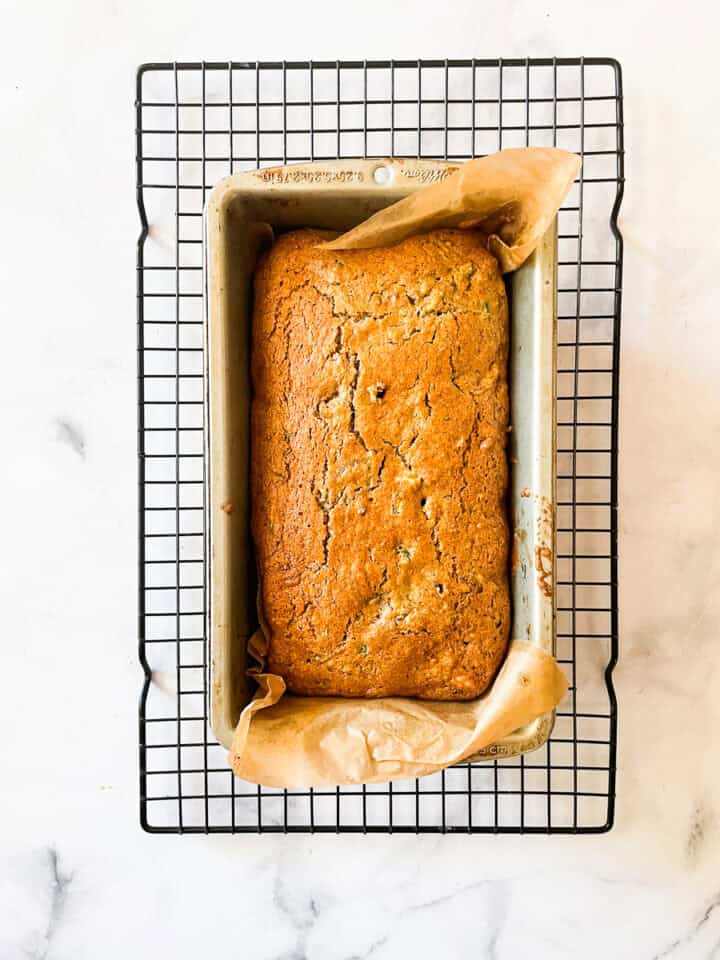 A loaf of gluten-free zucchini bread cools in a pan on a rack.