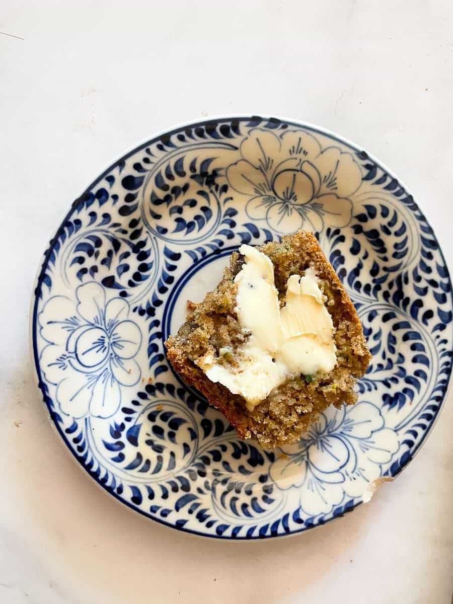 A piece of gluten-free zucchini bread on a plate spread with butter.