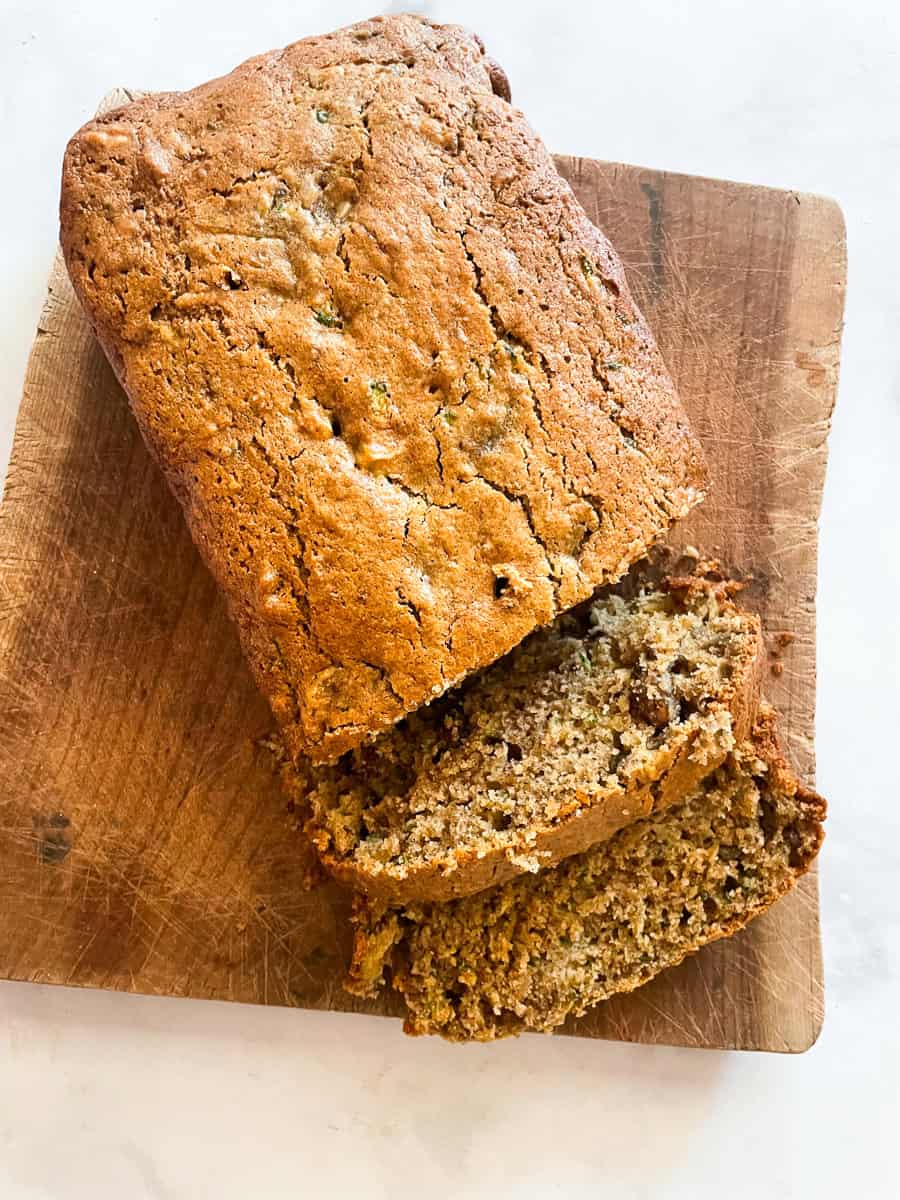 A wooden cutting board with a loaf of gluten-free zucchini bread.