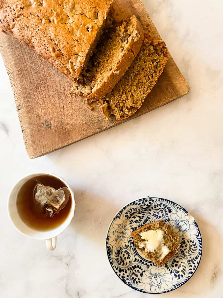 A sliced gluten-free zucchini bread loaf with a slice on a plate and a cup of tea.