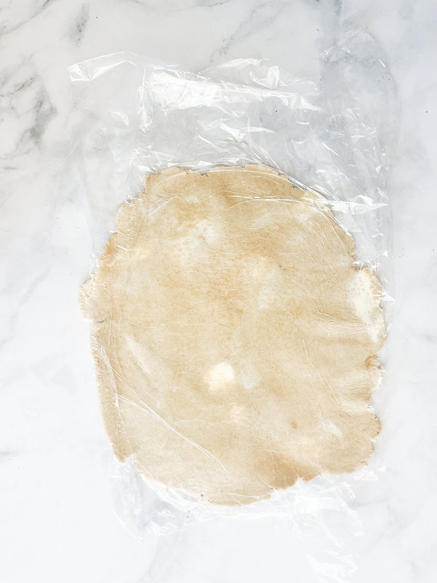 A gluten free crust is rolled out between sheets of plastic wrap.