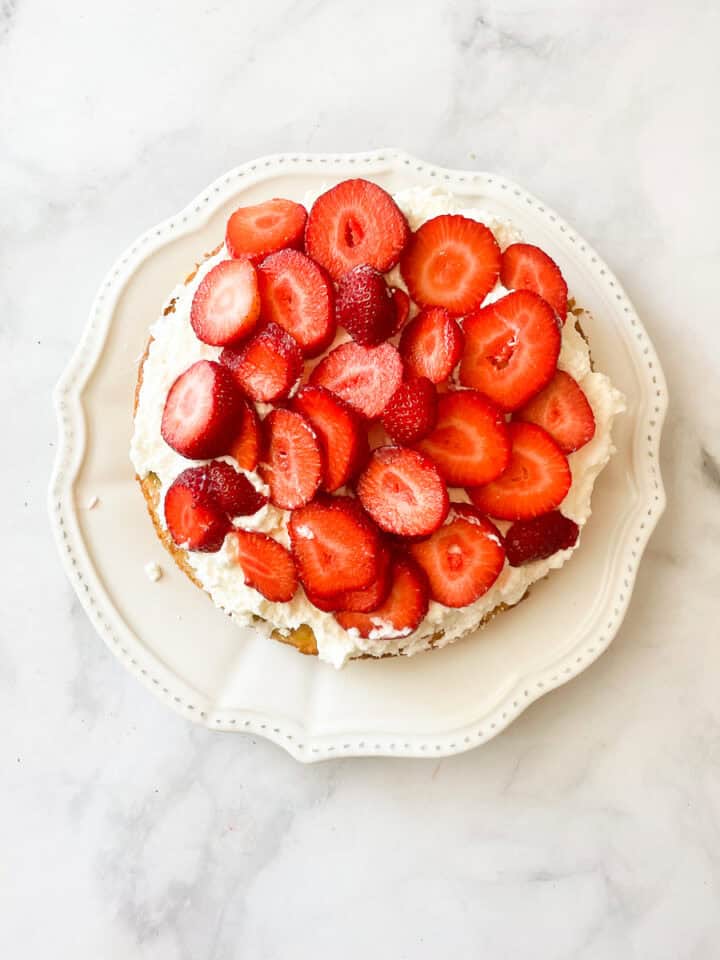 Strawberries and whipped cream on top of gluten free strawberry shortcake cake.