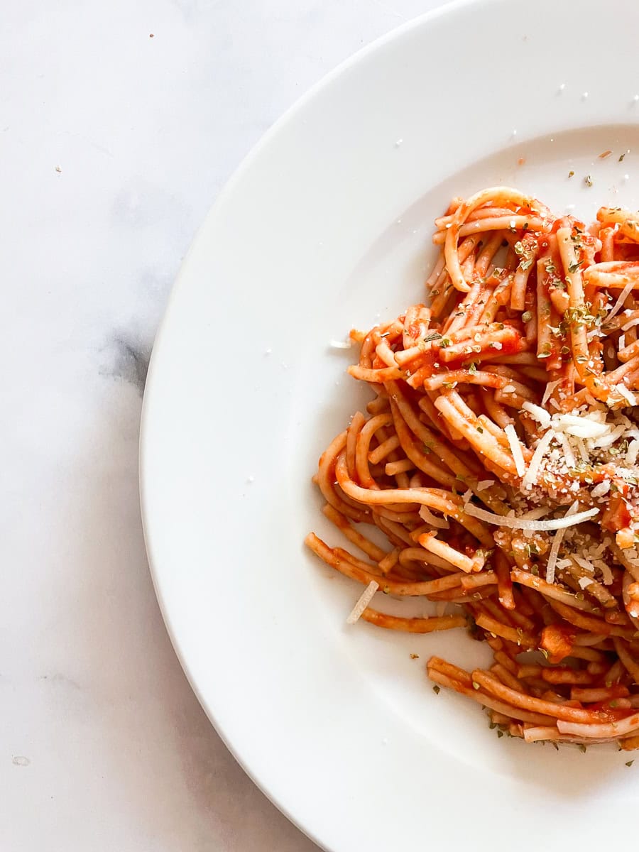 Half of a white plate holds spaghetti with simple tomato sauce.