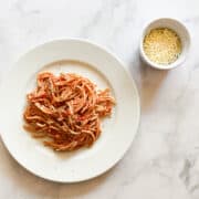 Spaghetti with simple tomato sauce on a plate with a bowl of cheese next to it.