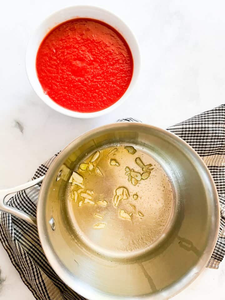 Garlic cooks in olive oil with pureed tomatoes next to the pot.