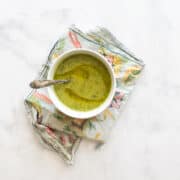 A bowl of zucchini soup on a napkin with a spoon in it.