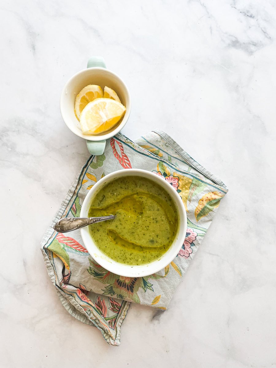 Lemon wedges are shown next to a bowl of zucchini soup with a spoon in it.