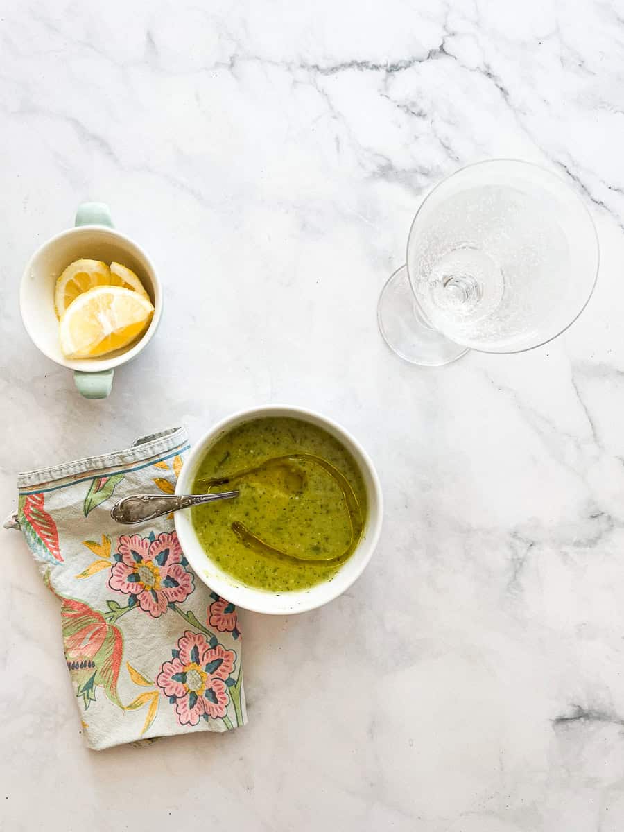 Lemon wedges are shown next to a bowl of zucchini soup with a spoon in it.