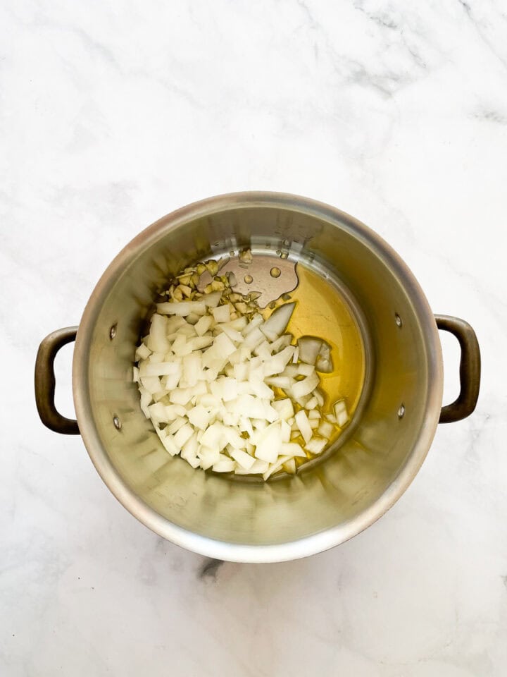 Garlic and onion are added to olive oil in a soup pot.