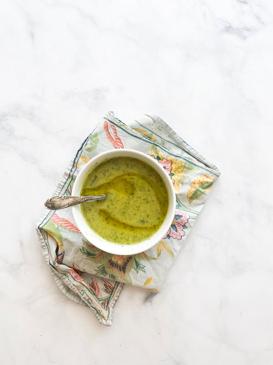 A bowl of zucchini soup on a napkin with a spoon in it.